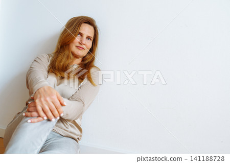 Portrait middle-aged blonde woman sitting on floor Portrait middle-aged blonde woman sitting on floor 141188728