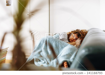 young woman lies on leather sofa covered with warm cozy blanket young woman lies on leather sofa covered with warm cozy blanket 141188793