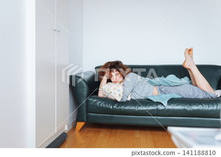 young red-haired woman relaxing on leather sofa 141188810