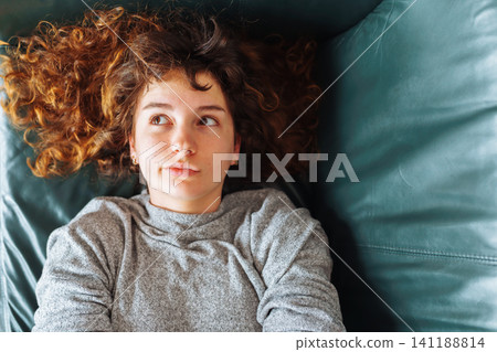 young red-haired woman relaxing on leather sofa young red-haired woman relaxing on leather sofa 141188814