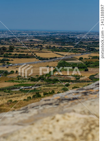Panoramic view of Malta countryside with golden fields, highway and distant town from old stone wall in hot summer Panoramic view of Malta countryside with golden fields, highway and distant town from old stone wall in hot summer 141188897