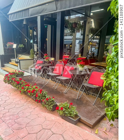 Cozy outdoor cafe terrace with red cushioned chairs bistro tables and blooming geranium flowers on charming city sidewalk Cozy outdoor cafe terrace with red cushioned chairs bistro tables and blooming geranium flowers on charming city sidewalk 141188907
