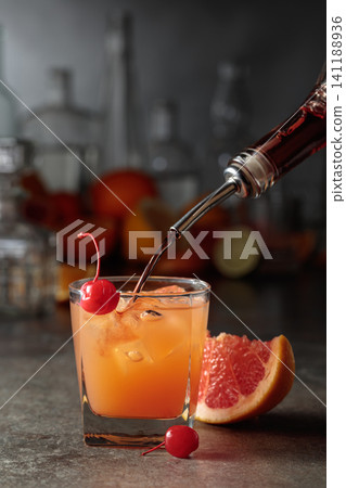 Strong alcohol is poured into a glass with ice and grapefruit juice. 141188936