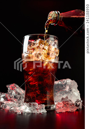 Sparkling cola is poured from a bottle into a misted glass with ice. 141188950