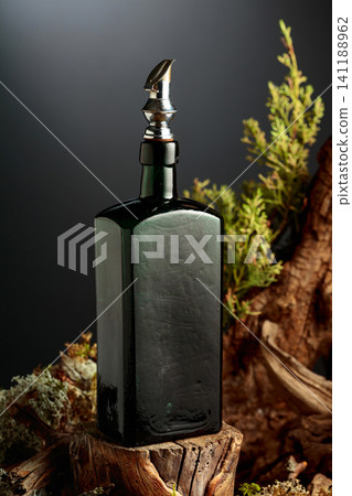 Vintage bottle of gin or herbal bitter, set among juniper branches, weathered driftwood and forest moss. Vintage bottle of gin or herbal bitter, set among juniper branches, weathered driftwood and forest moss. 141188962