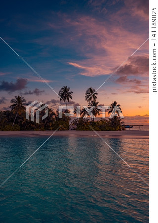 Tropical island silhouette with palm trees at purple sunset, vertical seascape. Dramatic pink and violet clouds reflecting in calm dark ocean at dusk. Moody romantic twilight scene for travel art Tropical island silhouette with palm trees at purple sunset, vertical seascape. Dramatic pink and violet clouds reflecting in calm dark ocean at dusk. Moody romantic twilight scene for travel art 141189025