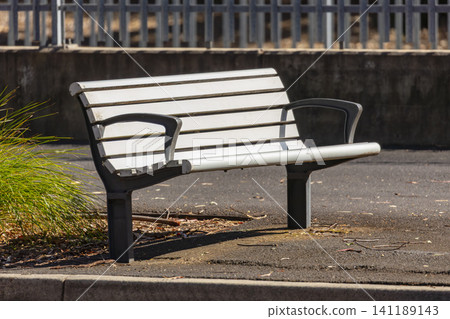 A public bench seat located on a footpath near a road and bus stop A public bench seat located on a footpath near a road and bus stop 141189143