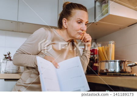 middle-aged woman prepares a recipe for lunch in her home kitchen 141189173