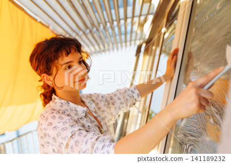 young woman washes windows on terrace 141189232