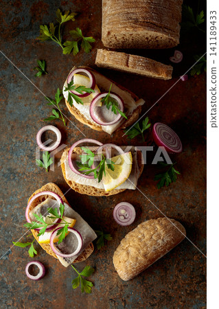 Open sandwiches with herring filet, red onion, lemon, and parsley. Open sandwiches with herring filet, red onion, lemon, and parsley. 141189433
