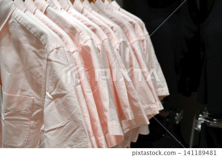 Row of pale pink shirts on hangers in retail clothing store for summer sales display and apparel banner background 141189481