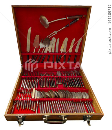 A vintage wooden briefcase is open to show a luxury cutlery set arranged neatly inside. The set features shiny silver pieces with wooden handles on a bright red velvet background. A vintage wooden briefcase is open to show a luxury cutlery set arranged neatly inside. The set features shiny silver pieces with wooden handles on a bright red velvet background. 141189712