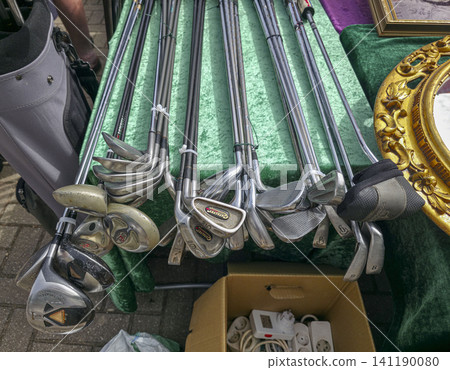XALO, SPAIN - JUNE 20, 2026.A variety of secondhand golf clubs and irons sit on a green velvet table in an outdoor market. Each club is placed neatly, showing interest from shoppers nearby. XALO, SPAIN - JUNE 20, 2026.A variety of secondhand golf clubs and irons sit on a green velvet table in an outdoor market. Each club is placed neatly, showing interest from shoppers nearby. 141190080