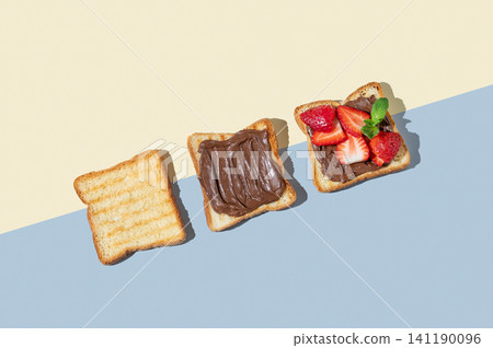 Three toasted slices with chocolate cream and strawberries on a yellow and blue isolated background Three toasted slices with chocolate cream and strawberries on a yellow and blue isolated background 141190096