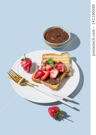 Toasted bread with chocolate cream and strawberry on a white plate on a blue background Toasted bread with chocolate cream and strawberry on a white plate on a blue background 141190098
