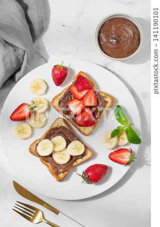 Toasted bread with chocolate cream, banana and strawberry on a plate on a marble background 141190101