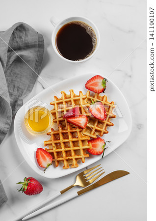 Belgian waffles with fresh strawberries and honey on a white plate on  a marble background 141190107