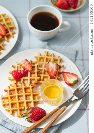Belgian waffles with fresh strawberries and honey on a white plate on  a blue tile background 141190109