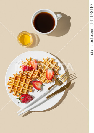 Belgian waffles with fresh strawberries and honey on a white plate on  a yellow background 141190110