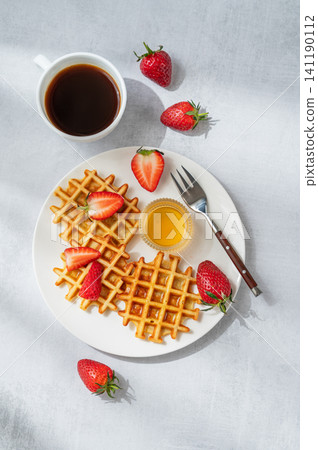 Belgian waffles with fresh strawberries and honey on a white plate on a concrete background Belgian waffles with fresh strawberries and honey on a white plate on a concrete background 141190112