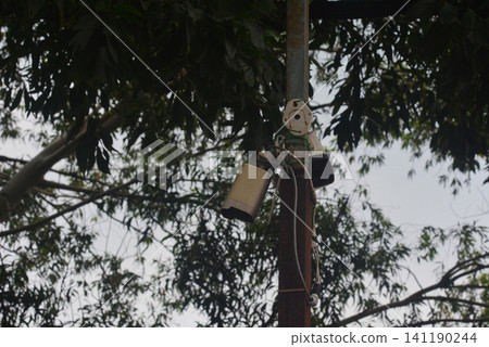 Security camera mounted on pole surrounded by green foliage and branches 141190244
