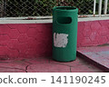 Green cylindrical public trash bin set against a pink hexagonal textured wall 141190245
