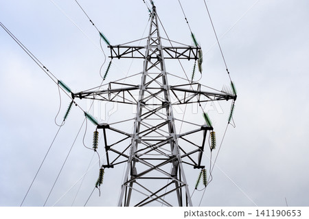 High-voltage power line tower rises against a cloudy sky. Steel lattice structure of the transmission line High-voltage power line tower rises against a cloudy sky. Steel lattice structure of the transmission line 141190653