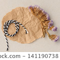 A composition of dried flower sprigs and black and white lace on a sheet of crumpled craft paper 141190738