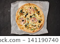 Round pizza with bacon, chicken, olives and cheese on parchment and dark background 141190740