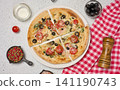 Appetizing pizza cut into pieces on a round white plate with tomatoes, olives, spices and a wooden grinder 141190743