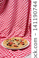 Pizza with cheese, tomatoes and olives on a white plate standing on a checkered red tablecloth 141190744