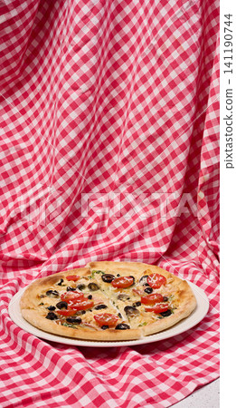 Pizza with cheese, tomatoes and olives on a white plate standing on a checkered red tablecloth Pizza with cheese, tomatoes and olives on a white plate standing on a checkered red tablecloth 141190744