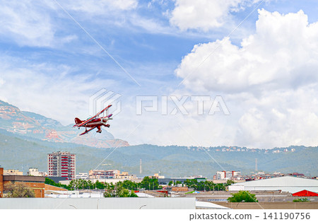 A red aerobatic biplane performing air shows in a blue sky with white clouds. Classic airplanes 141190756
