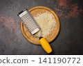 A pile of grated cheese and a metal grater on a round wooden board, dark textured background 141190772