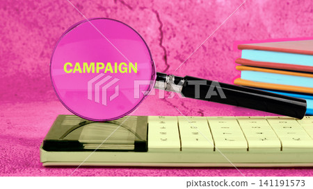 A magnifying glass highlights the word campaign on a calculator that sits on a colorful stack of notebooks on a desk in a bright setting A magnifying glass highlights the word campaign on a calculator that sits on a colorful stack of notebooks on a desk in a bright setting 141191573