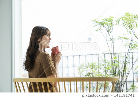 A young woman drinking coffee by the window on a rainy day. A young woman drinking coffee by the window on a rainy day. 141191741