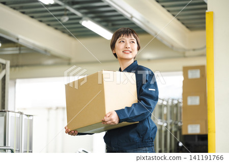 一位身穿工作服的年輕女子在物流倉庫工作 一位身穿工作服的年輕女子在物流倉庫工作 141191766