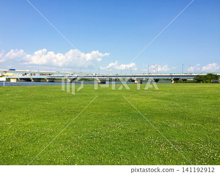 A vast lawn and a bridge over the Arakawa River embankment, under a summer blue sky. A vast lawn and a bridge over the Arakawa River embankment, under a summer blue sky. 141192912