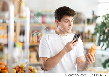 Male buyer checks suitability - scans QR code on jar of hot sauce label in grocery store 141193267