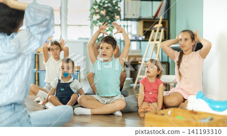 Children repeating teacher's movements while sitting on floor Children repeating teacher's movements while sitting on floor 141193310