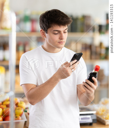 Guy scanning barcode on soy sauce using phone in food store Guy scanning barcode on soy sauce using phone in food store 141193315