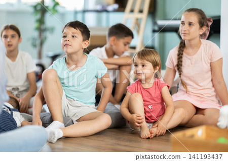 Group of children is sitting on floor, listening to teacher in kindergarten 141193437
