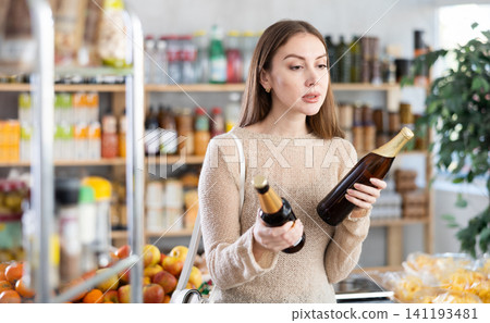 Pensive young woman shopping for beer in grocery store Pensive young woman shopping for beer in grocery store 141193481