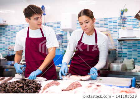 Proficient sellers processing seabass on table board in fish store Proficient sellers processing seabass on table board in fish store 141193529