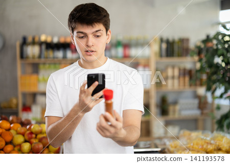 Guy scanning QR code on bottle cardamom label in grocery department of supermarket Guy scanning QR code on bottle cardamom label in grocery department of supermarket 141193578