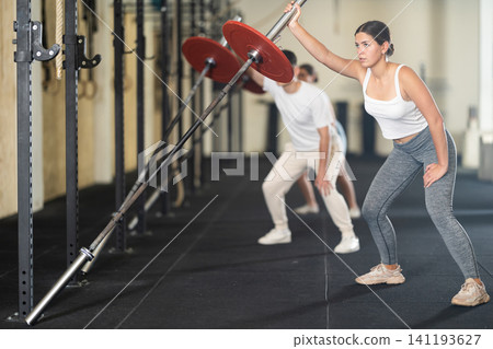 Young woman training with barbell with one arm Young woman training with barbell with one arm 141193627