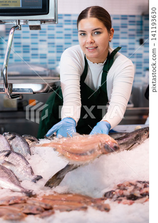 Female seller shows hands fish lenguadina on counter in supermarket Female seller shows hands fish lenguadina on counter in supermarket 141193630