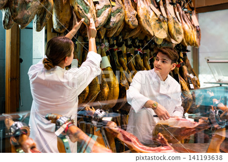 Young man and woman selling spanish jamon at counter Young man and woman selling spanish jamon at counter 141193638