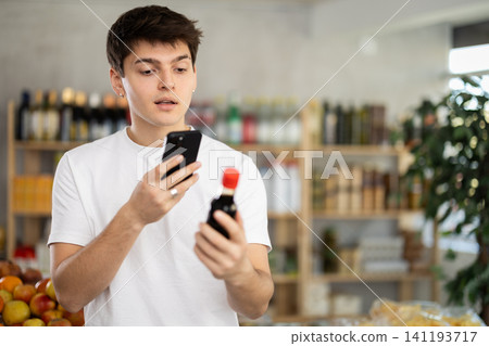 In shop young man scans QR code and take reading on soy sauce package using phone camera In shop young man scans QR code and take reading on soy sauce package using phone camera 141193717