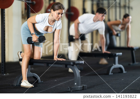 Young woman training with dumbbells on bench Young woman training with dumbbells on bench 141193822